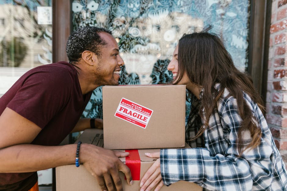 Two removal personnel from Removal Companies Streatham are engaged in the loading process of a home relocation, standing at the rear of a white panel van with its side and rear doors open. They are ca